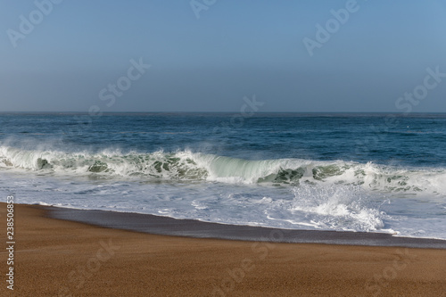 Foamy Atlantic ocean wave on Nazare city beach, Portugal.