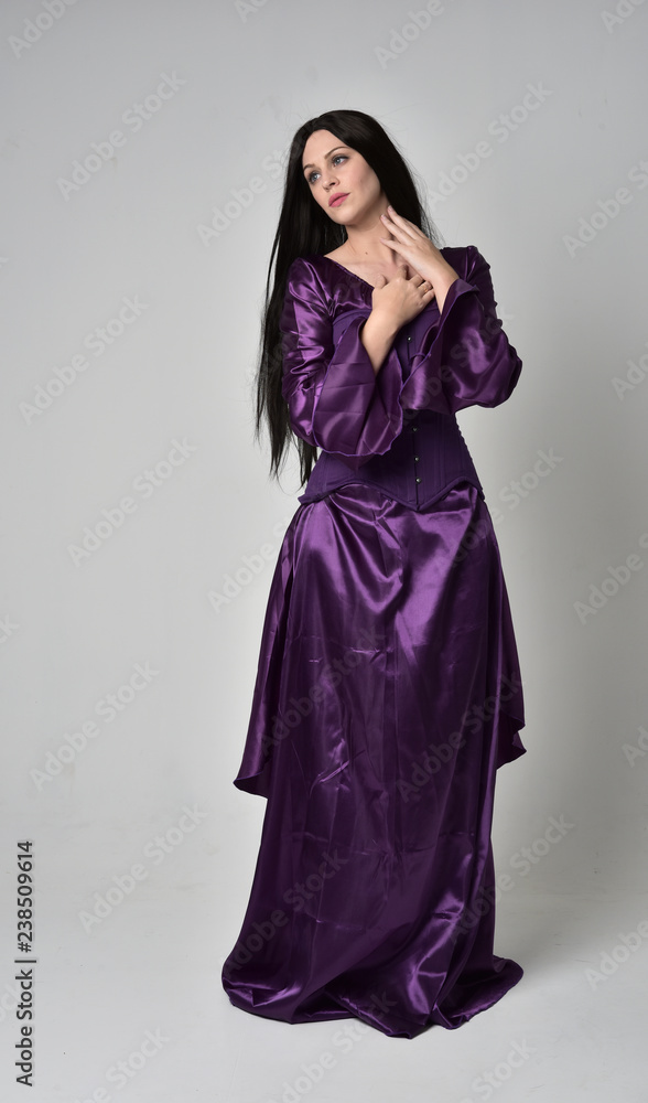 full length portrait of beautiful girl with long black hair, wearing purple fantasy medieval gown. standing pose on grey studio background. full length portrait of beautiful girl with long black hair, wearing purple fantasy medieval gown. standing pose on grey studio background.