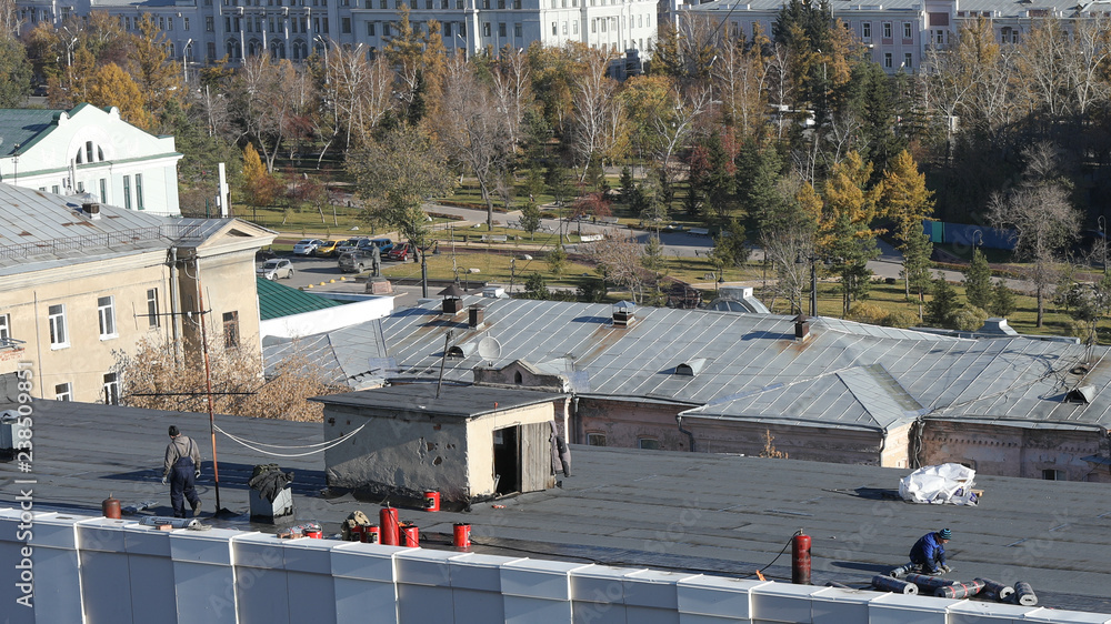 OMSK, RUSSIA - october 12, 2018: construction workers install roll of roofing insulation material during repair of waterproofing a flat roof OMSK, RUSSIA - october 12, 2018: construction workers install roll of roofing insulation material during repair of waterproofing a flat roof