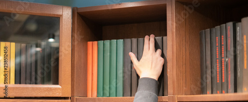 person hand searching for a book at home on a book shelf n
