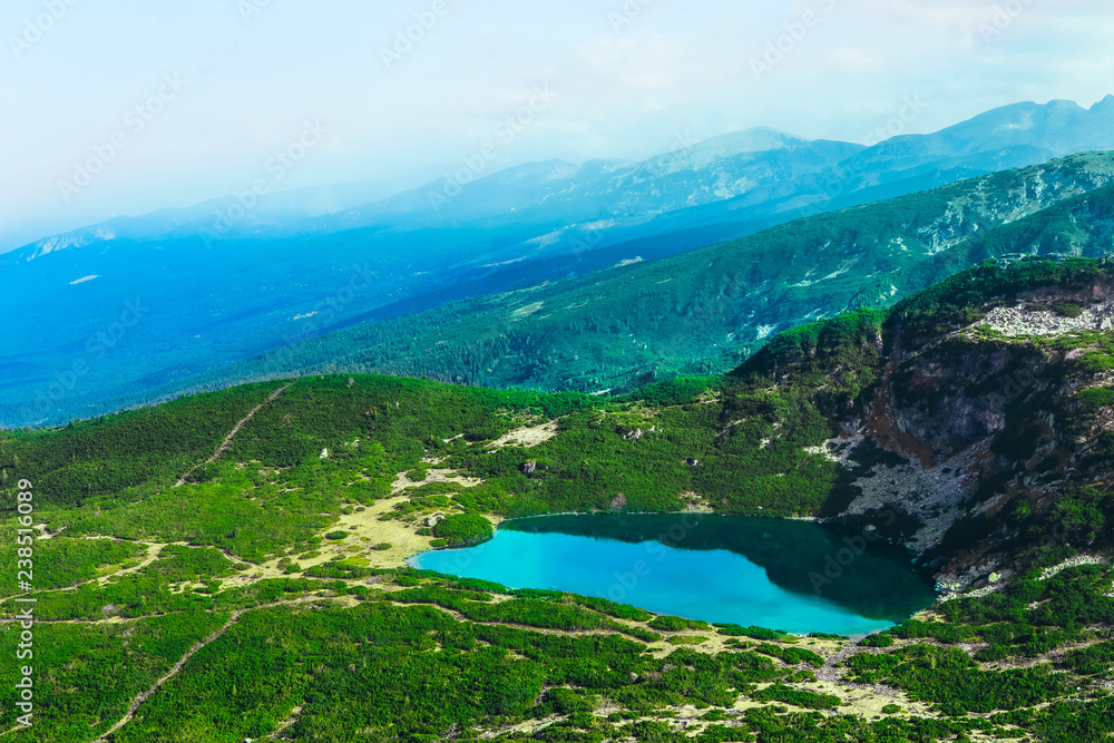 Alpine mountain lake, green meadows, hiking trail. Amazing valley landscape.