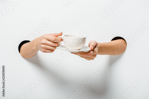 cropped image of woman holding cup of coffee and plate through holes on white
