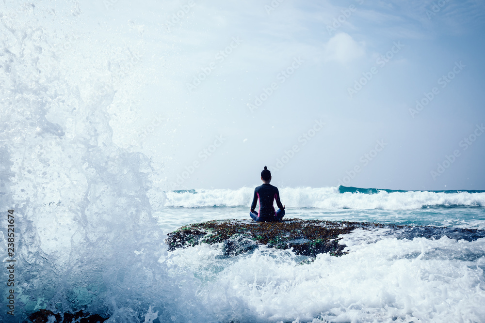 Naklejka premium Woman meditation at the seaside cliff edge facing the coming strong sea waves