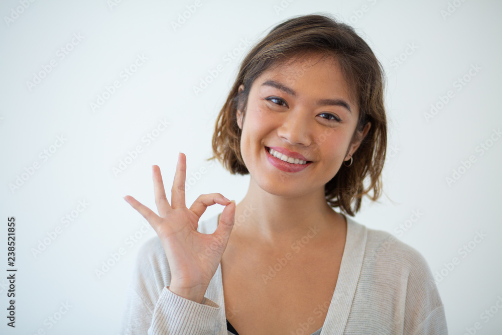 Portrait of happy young woman gesturing alright. Asian girl showing satisfaction sign. Success concept Portrait of happy young woman gesturing alright. Asian girl showing satisfaction sign. Success concept