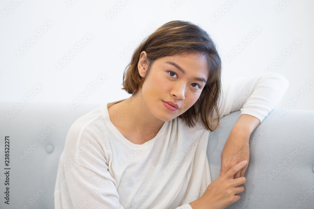 Portrait of serious teenage girl sitting on coach. Young Asian woman posing at home looking at camera. Young woman concept Portrait of serious teenage girl sitting on coach. Young Asian woman posing at home looking at camera. Young woman concept