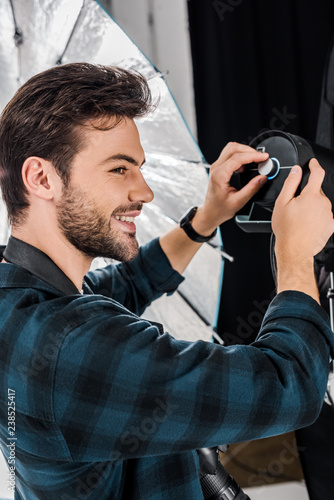handsome smiling young photographer working with professional lighting equipment in photo studio