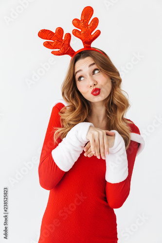 Portrait of adorable woman 20s wearing Santa Claus red costume and deer ears smiling and standing, isolated over white background