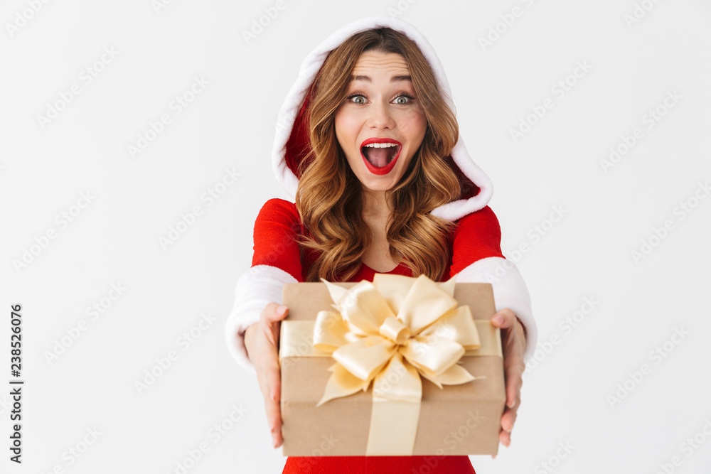 Portrait of beautiful woman 20s wearing Santa Claus red costume smiling and holding present box, isolated over white background Portrait of beautiful woman 20s wearing Santa Claus red costume smiling and holding present box, isolated over white background