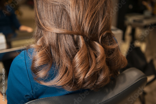 Beautiful brunette curls in luxury beauty salon. Closeup on brown hair made by hairdresser. Young girl in leather black chair with fabulous styling.