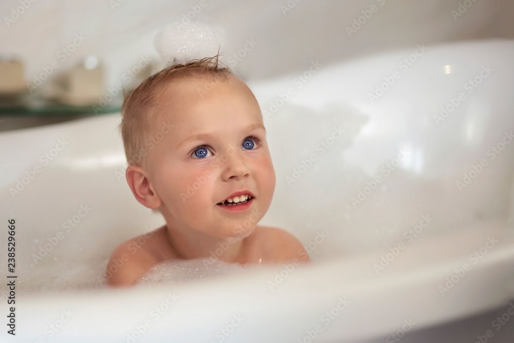 Cute caucasian baby boy with navy blue eyes in the bathtube, with foam bubbles on his head and around. Indoors, close up portrait of pretty baby, white background, copy space. Cute caucasian baby boy with navy blue eyes in the bathtube, with foam bubbles on his head and around. Indoors, close up portrait of pretty baby, white background, copy space.