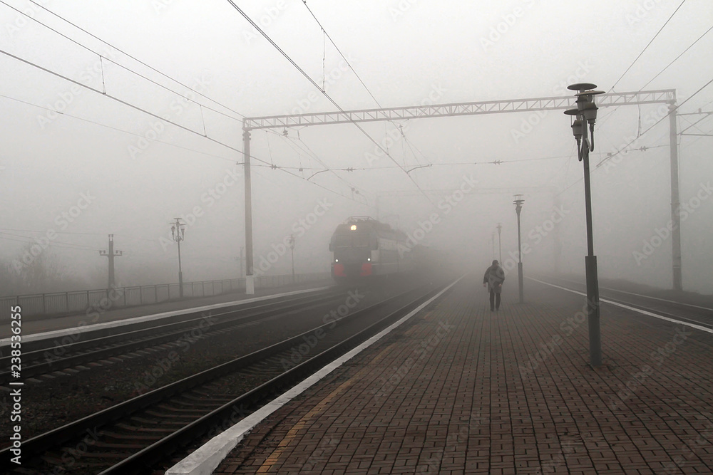 The train leaves the fog, next to the man on the platform.