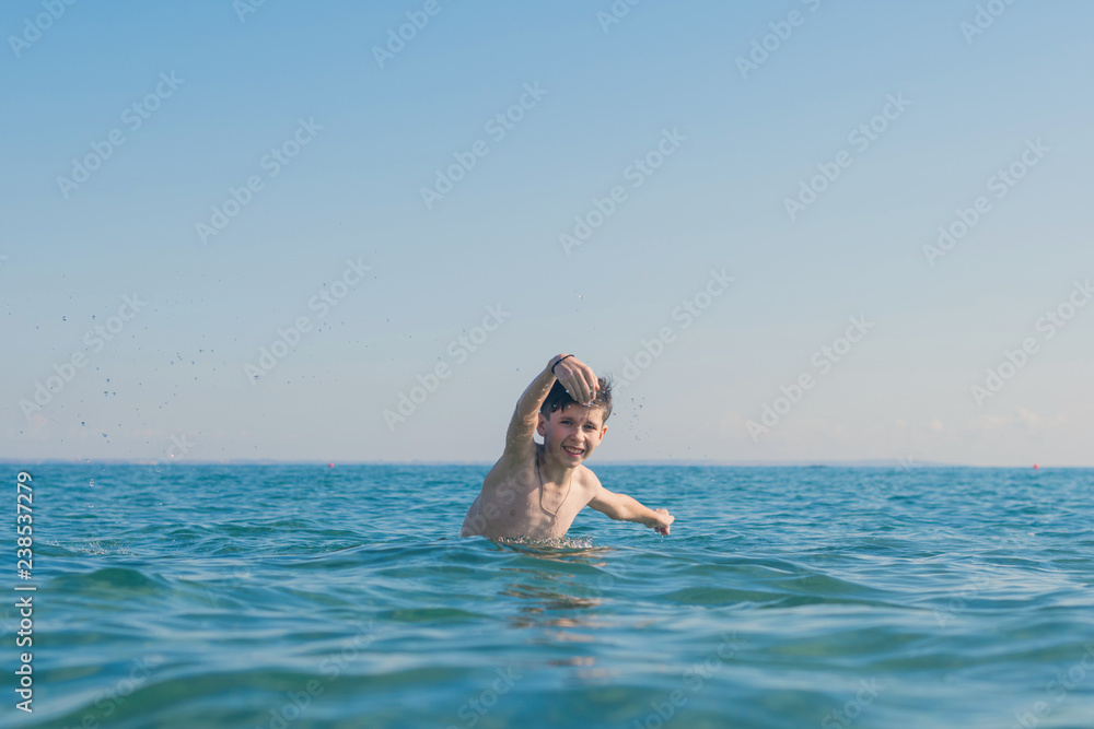 Happy and smiling teen boy swimming in the sea. Travel and summer concept