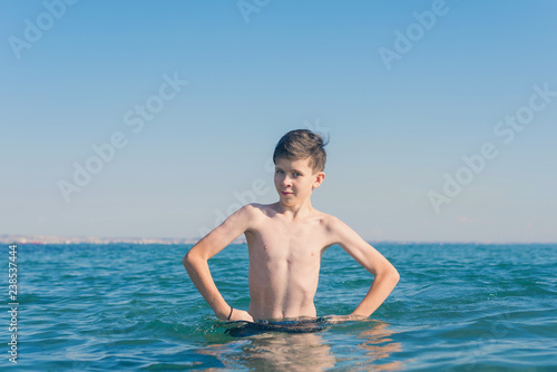 13 years old boy holding hands on hips and outraged standing in the sea waves. Concept