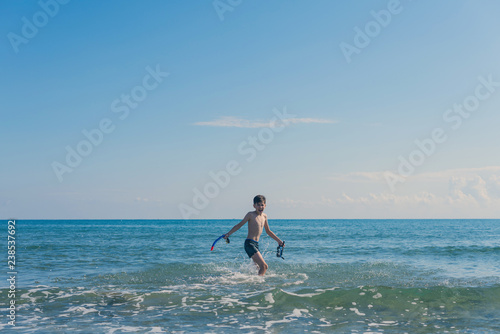 Happy teen boy with snorkeling mask and tube running   n the wave of the sea during summer vacation in the tropical resort town