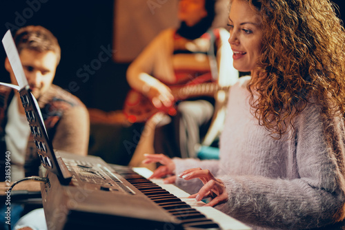 Guitarist showing woman how to play clavier. Selective focus on woman. Home studio interior.