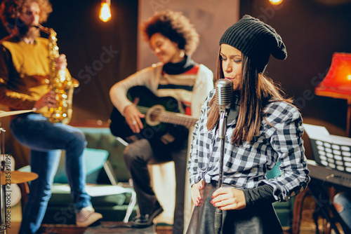 Band practice in home studio. Woman singing while rest of the band playing instruments.