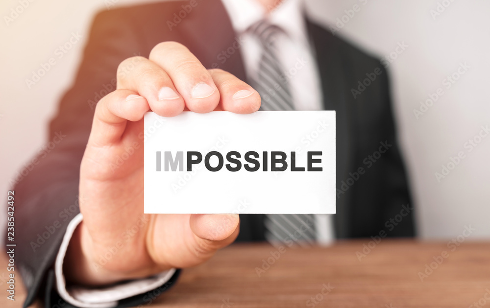 Businessman holding a card with text Impossible Businessman holding a card with text Impossible