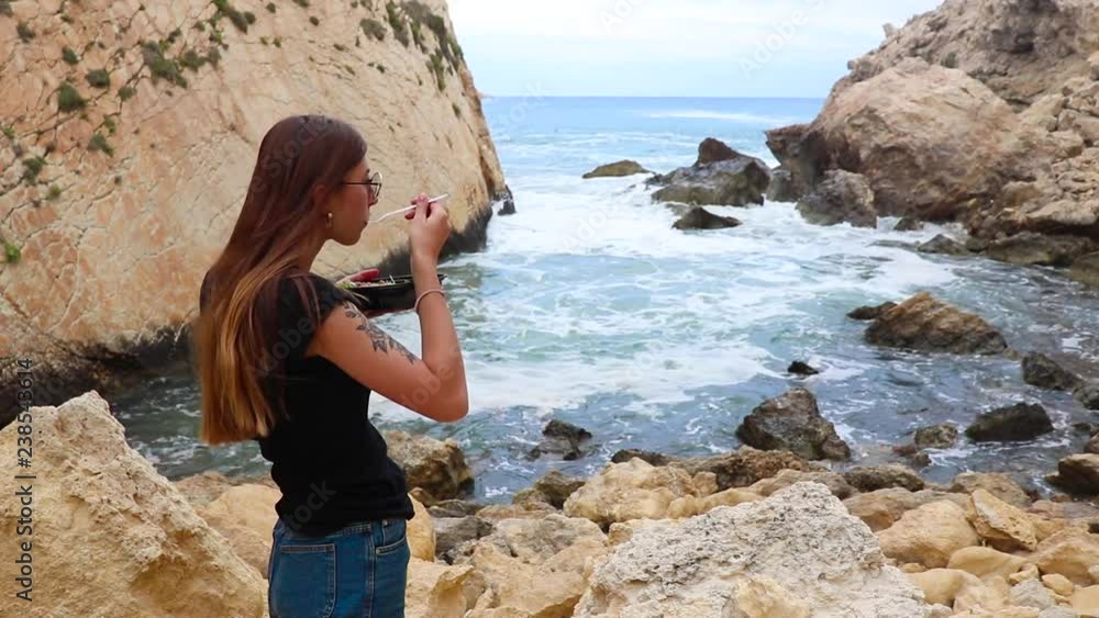 Young woman having a dinner on the background of the sea and stones on Malta Young woman having a dinner on the background of the sea and stones on Malta