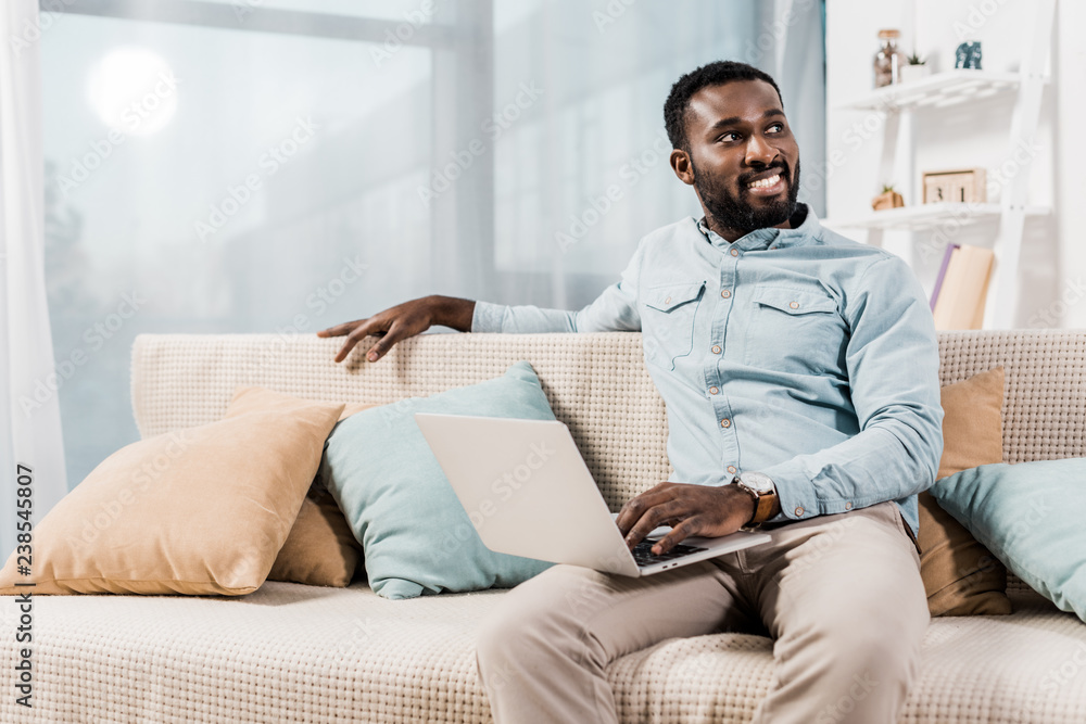 Fototapeta premium african american freelancer sitting on couch in living room and looking away