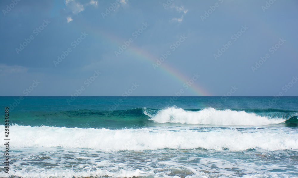 Beautiful view of the raibow over the sea and waves braking on the shore