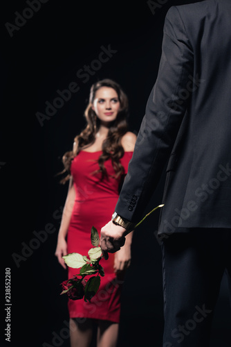 selective focus of man holding rose with woman in red dress on background isolated on black