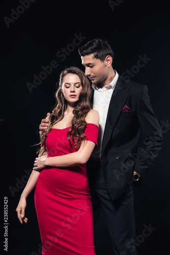 handsome man embracing beautiful woman in red dress isolated on black