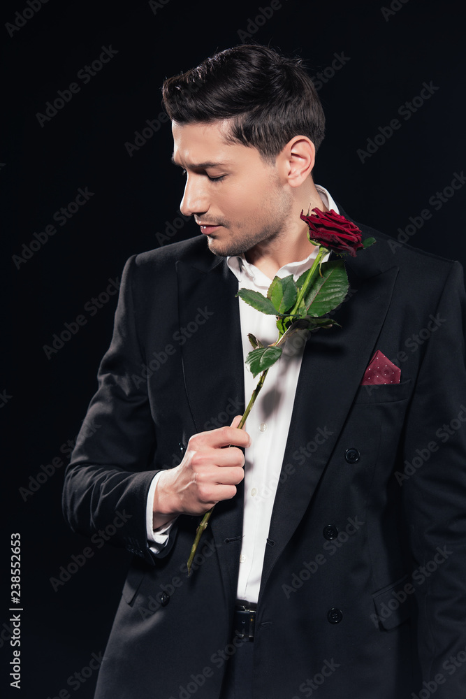 man in suit holding red rose and looking away isolated on black man in suit holding red rose and looking away isolated on black