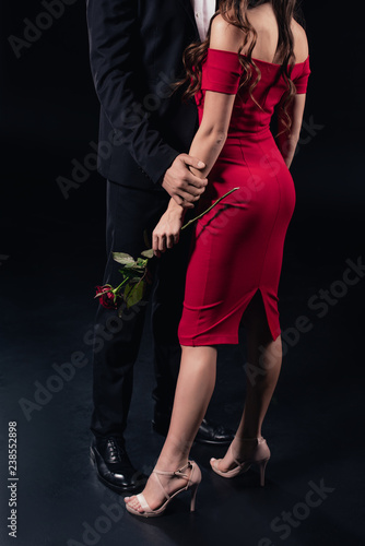 cropped view of man embracing woman in red dress holding rose isolated on black