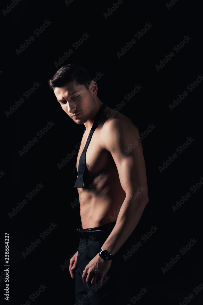 handsome shirtless man looking away and posing isolated on black