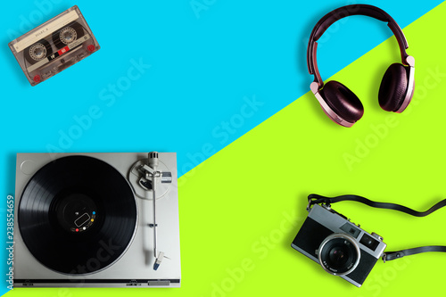 Old film camera, Old retro Vinyl record player or turntable, Over-Ear Headphone and cassette tape on a split yellow and blue background, gadgets for The 70-80-90's