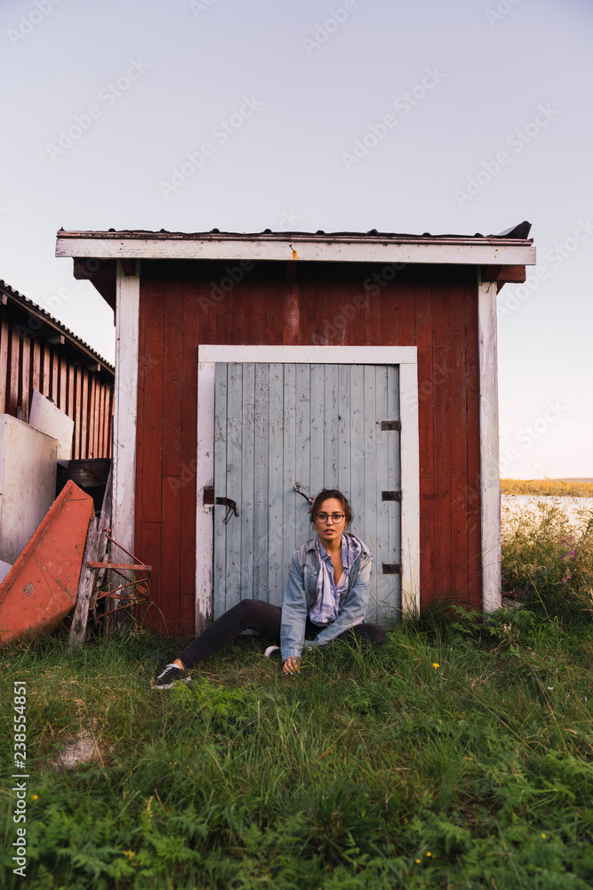 Portrait of a young woman sitting in grass in front of a wooden shack Portrait of a young woman sitting in grass in front of a wooden shack