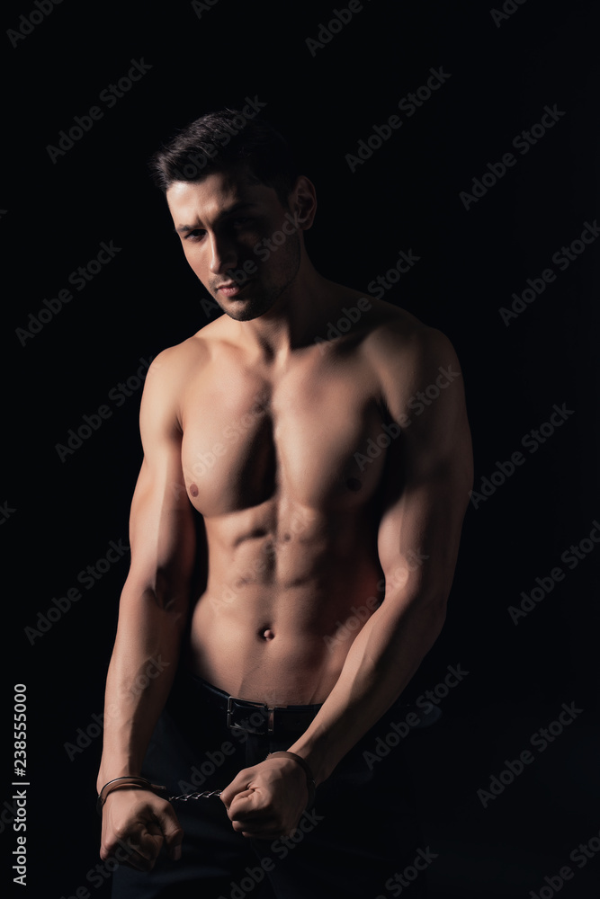 Fototapeta premium shirtless man in handcuffs looking at camera isolated on black