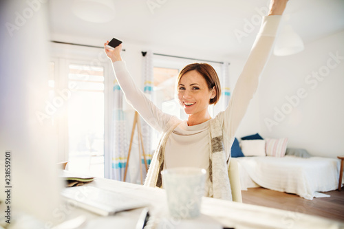 A happy young woman with outstretchced arms indoors  working in a home office.