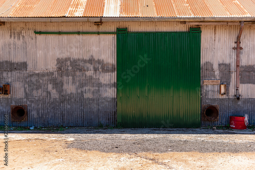 Metallic barn or deposit sliding door on green color with an old half cutted red barrel