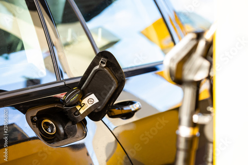 Fuel nozzle at a gas station with fuel tank cap on a car