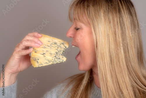 Blonde woman eating and enjoying a wedge of blue cheese