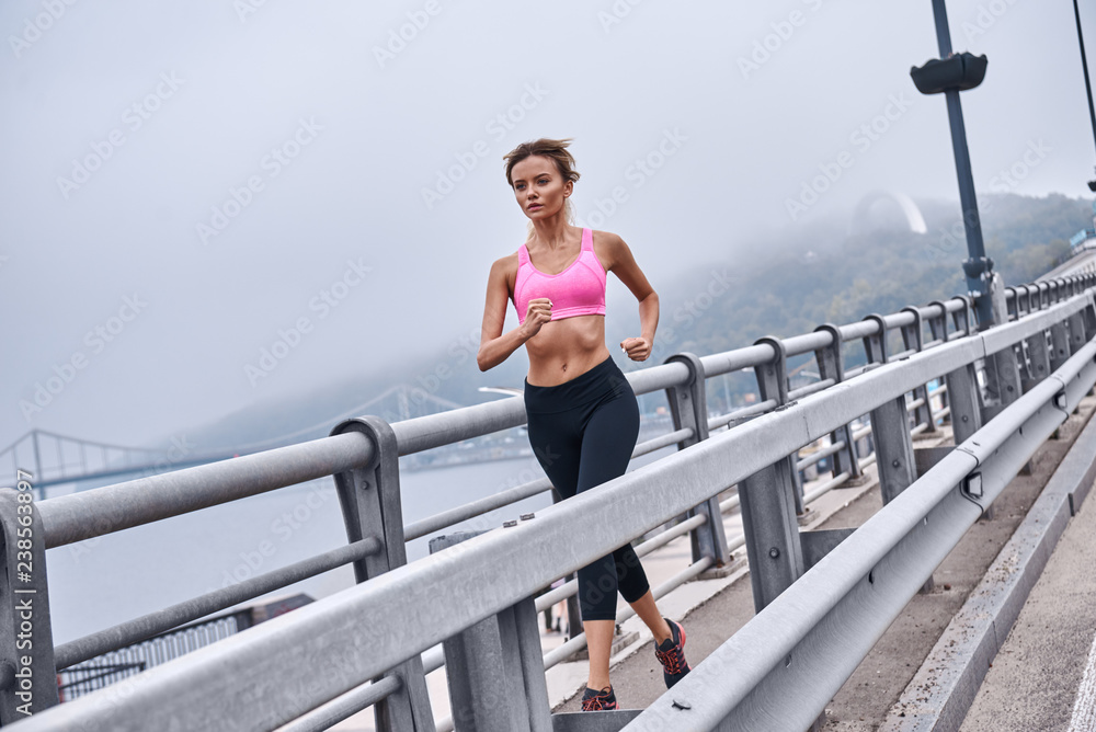 Always in great shape. Full length of young womanin sports clothing exercising while jogging on the bridge outdoors Always in great shape. Full length of young womanin sports clothing exercising while jogging on the bridge outdoors