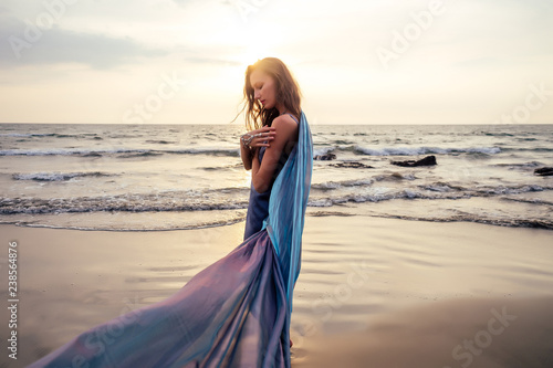 gorgeous style brunette young woman in blue chameleon dress long train standing on a rock near the sea, sand tropical on a rock.beautiful mermaid lonely melancholy waiting freedom and freelancing photo