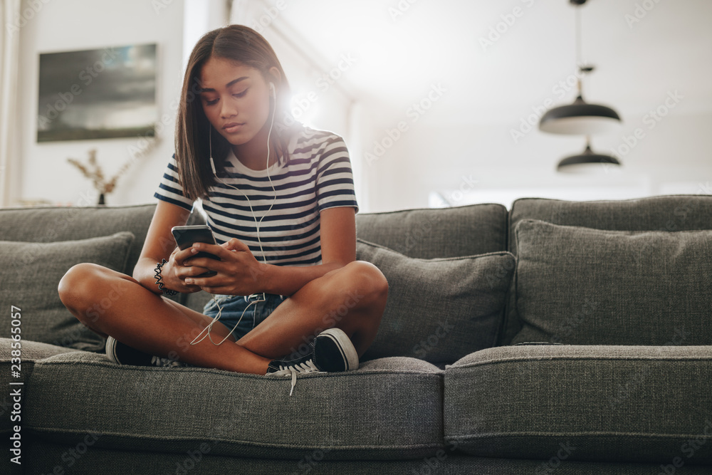 Girl listening to music sitting on couch - obrazy, fototapety, plakaty 