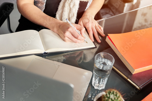 Woman s hands making notes on white spread notebook. Cactus and glass of water. Young woman or student working and writing on paper  space for text.