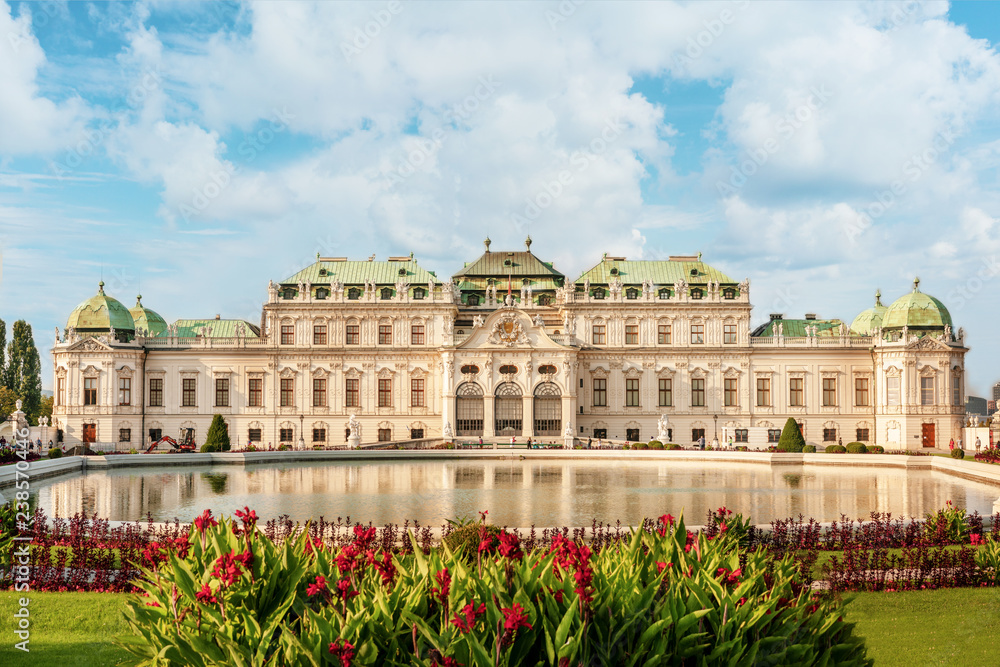 Belvedere palace at sunny day with reflection in a pond and flowers on foreground.