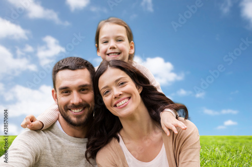 family and people concept - happy mother, father and little daughter over blue sky and grass background