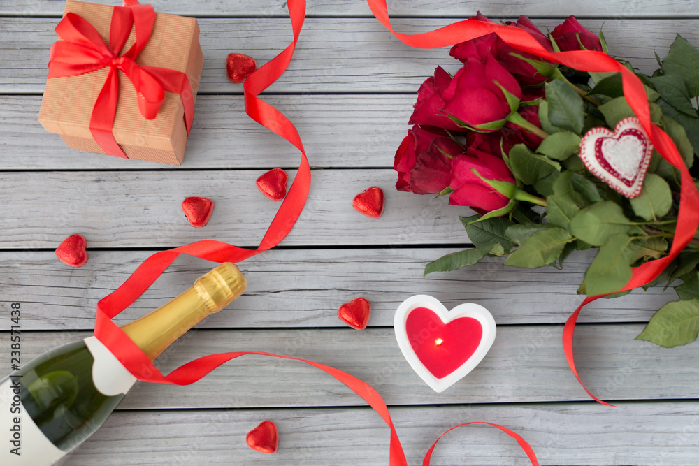 valentines day and holidays concept - close up of champagne, gift, red heart shaped chocolate candies, candle and red roses valentines day and holidays concept - close up of champagne, gift, red heart shaped chocolate candies, candle and red roses