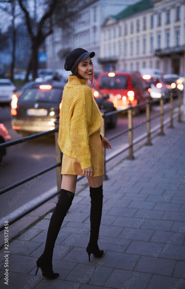 beautiful fashionable woman in bright yellow sweater and skirt and knee high heel boots walking and posing outdoors