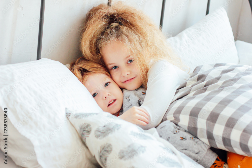 Little cute brother and sister in pajamas lie in bed, cozy morni