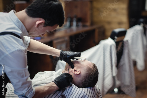 Hairdresser in black gloves shaves with a straight razor beard