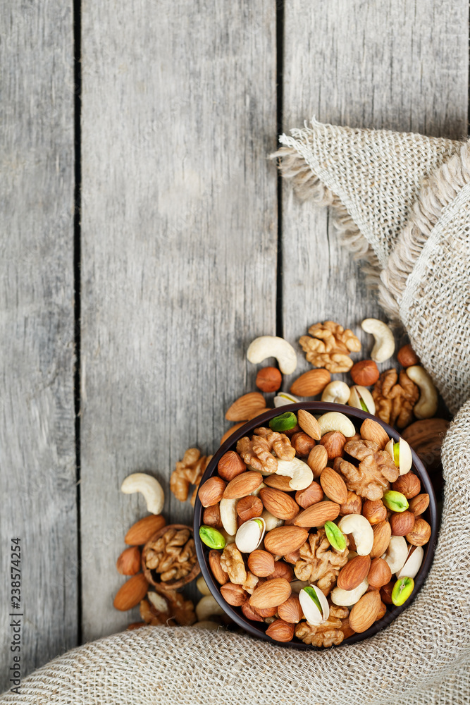 Wooden bowl with nuts on a wooden background, near a bag from burlap.