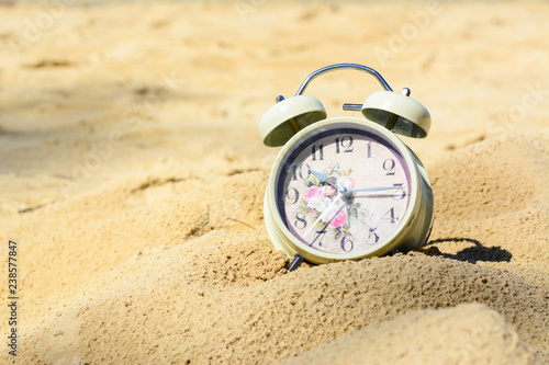 A retro alarm clock on a sand at the beach with golden sunlight. photo