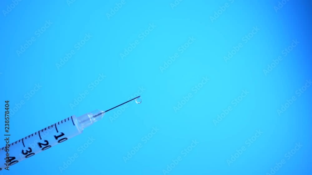 Syringe with drops closeup isolated on blue background. Medicine plastic vaccination equipment with needle. Liquid drug or narcotic or health care in hospital concept Syringe with drops closeup isolated on blue background. Medicine plastic vaccination equipment with needle. Liquid drug or narcotic or health care in hospital concept