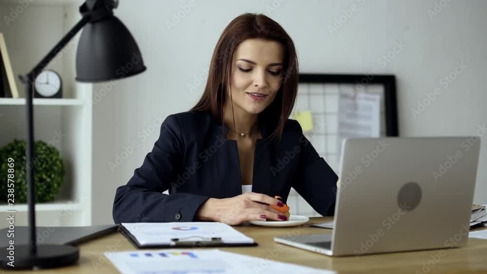 smiling businesswoman having lunch with delicious cupcake at table with laptop in office smiling businesswoman having lunch with delicious cupcake at table with laptop in office